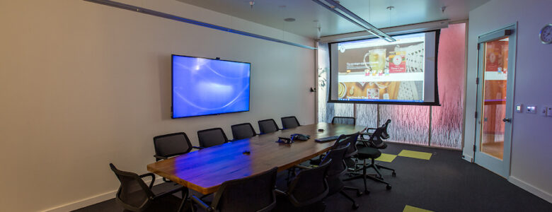 empty conference room table with on-wall TV and projector screen displays