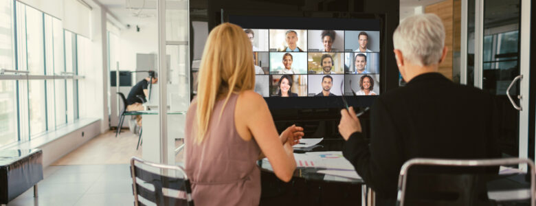 Two people sitting in front of a video conference display in a huddle space.